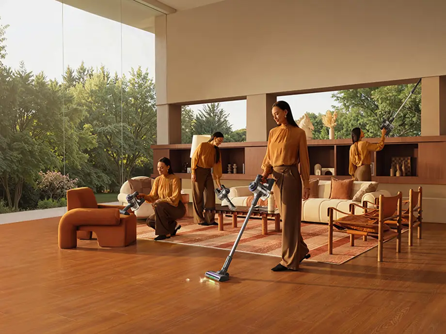 Woman using an upright vacuum cleaner to clean the floor, couch, and high shelves.