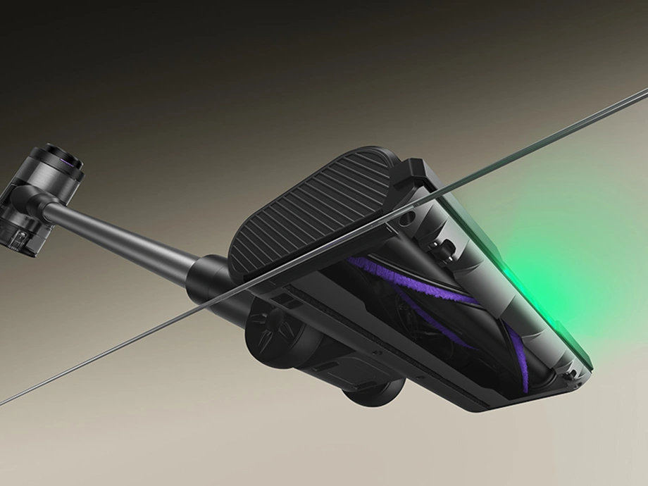 Close-up of the underside of an upright vacuum cleaner brush with a purple roller and green light.