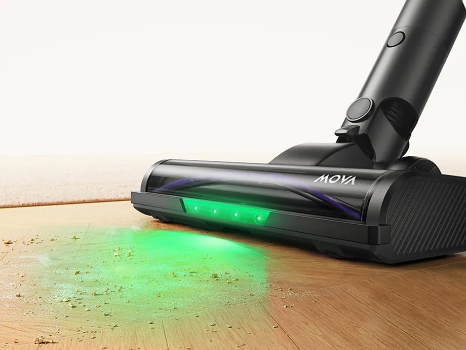 The brush of an upright vacuum cleaner illuminates dust particles on the floor with a green light.