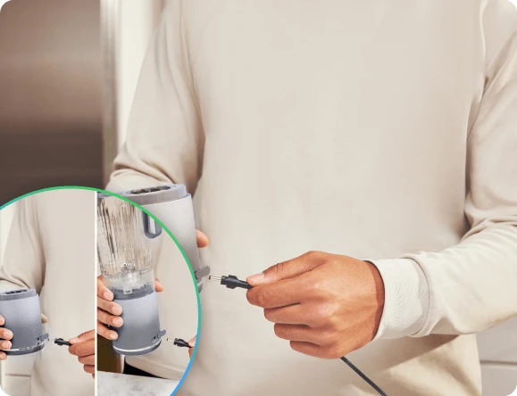 Руки вставляють штекер зарядного пристрою в порт на нижній частині блендера Ninja Blast Max BC251EU