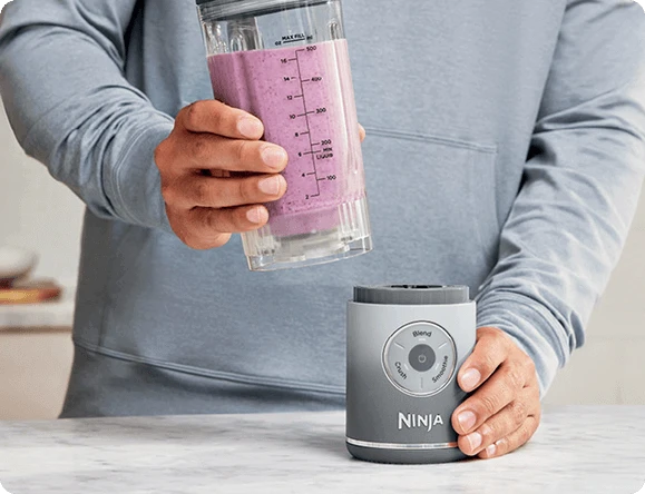 Руки виймають глечик, наповнений напоєм, з основи блендера