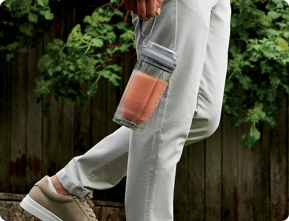 Чоловік іде з наповненим глечиком блендера в руці, тримаючи його за ремінь для перенесення