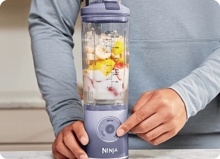 Чоловічі руки з вказівним пальцем на кнопці налаштувань блендера Ninja Blast Max BC251EU