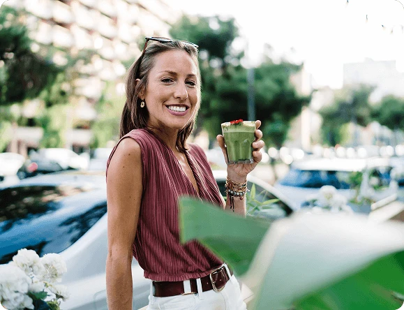 Усміхнена жінка п'є зелений напій у міському середовищі