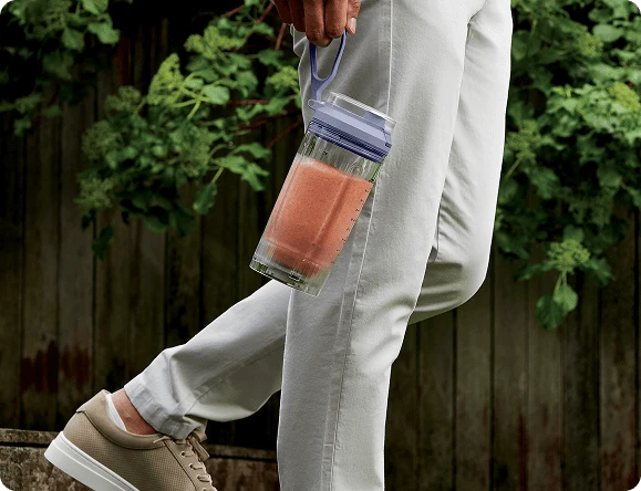 Чоловік іде з наповненим глечиком блендера в руці, тримаючи його за ремінь для перенесення