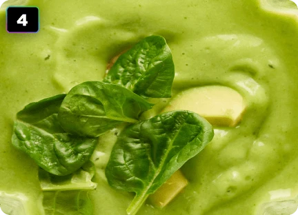 Крупний план густого зеленого напою з шматочками яблука та листям базиліка.