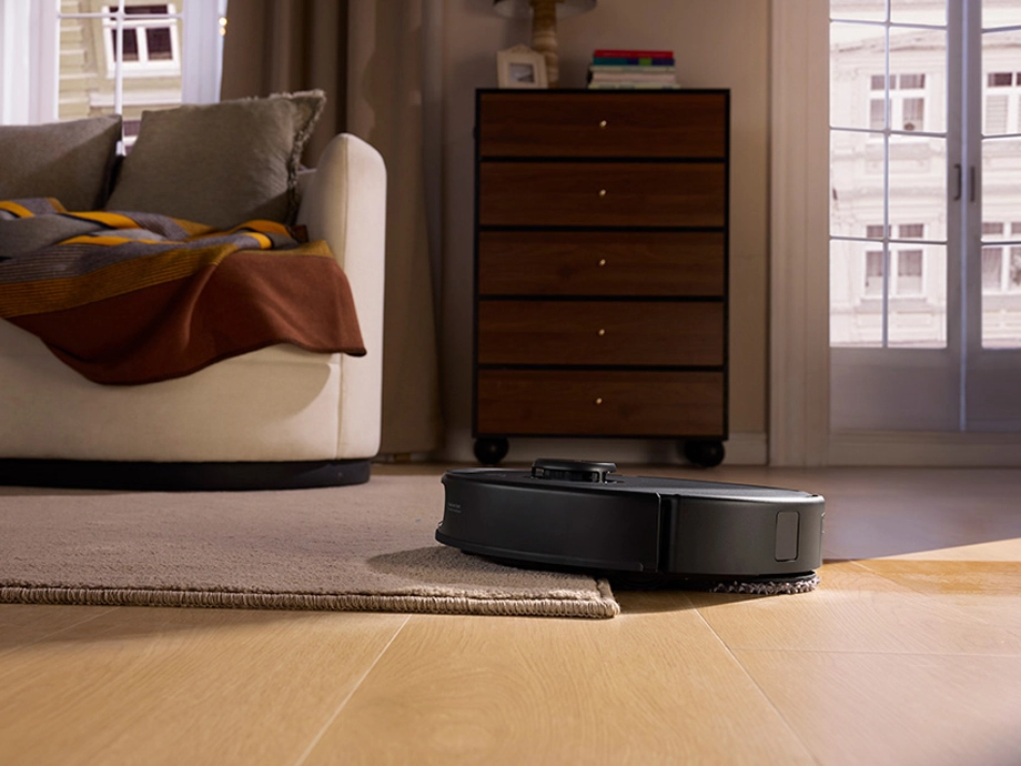 Робот-уборщик заезжает на ковер в гостиной перед диваном.