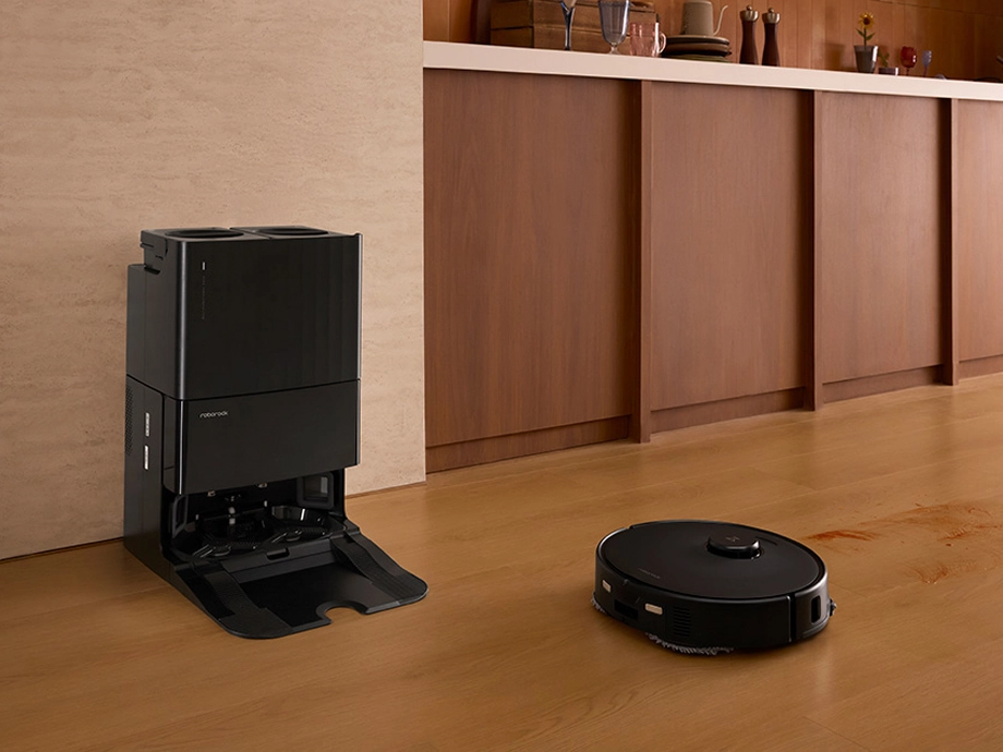 Робот-пылесос убирает пятно на деревянном кухонном полу, рядом с ним находится док-станция.