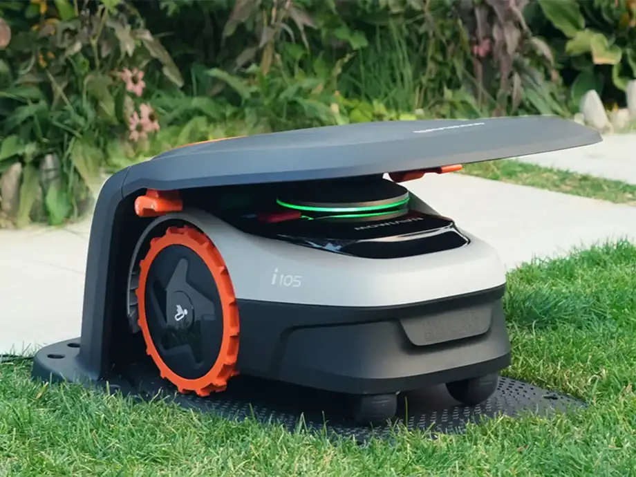 Роботизована газонокосарка стоїть на зеленій галявині в гаражі роботів.