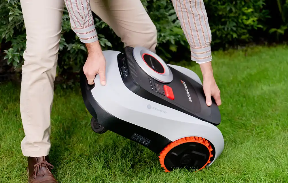 чоловік піднімає роботизовану газонокосарку з трави