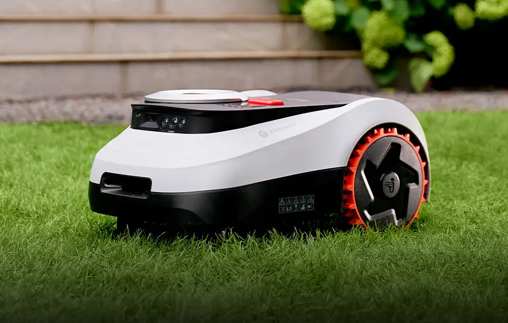 чорно-білий робот косить траву перед будинком, на задньому плані видно сходи