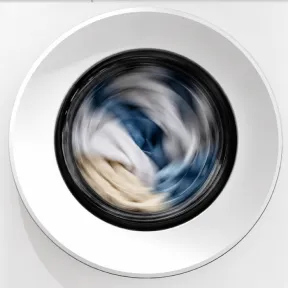 Zbliżenie na drzwi pralki Indesit z widocznym praniem obracającym się wewnątrz bębna.